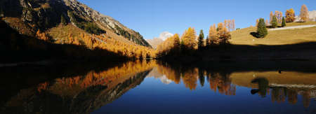 A panoramic shot of autumn forest and its reflection on the lakeの写真素材