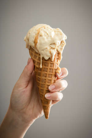 A hand holding a melty caramel ice-cream cone with bright backgroundの写真素材
