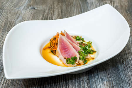 A closeup of raw meat with sliced vegetables and a sauce in a white modern plateの写真素材