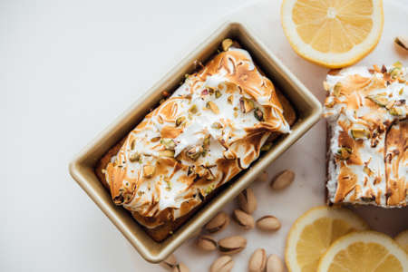 An overhead wide shot of tasty cake dessert with nuts and lemons on a white plate and white backgroundの写真素材