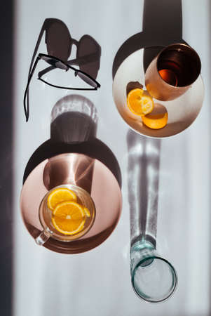 A top view of sunglasses, cup of tea, oranges, and an empty glass with their projected shadows on the white tableの写真素材
