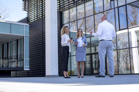 A caucasian senior businessman and two young businesswomen outside the building on a break
