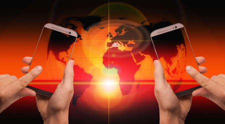 A closeup view of hands holding phones with a world map on the red and orange background