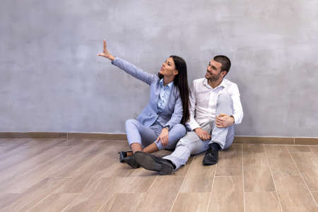 An excited young couple sitting on the floor of empty new apartment and planning arrangement