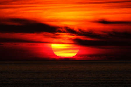 A beautiful shot of a sea and sun behind the clouds at sunset