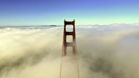 A beautiful aerial shot of the top of a bridge surrounded by clouds and blue sky in the background