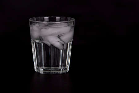 A closeup of a glass of water with ice isolated on a black backgroundの写真素材