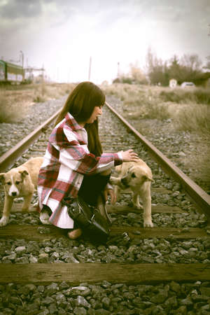 A vertical shot of a Caucasian female playing with dogs on the train tracksの写真素材