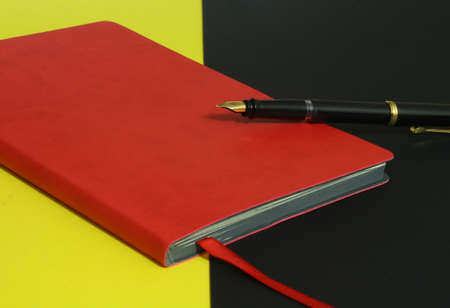 Red notebook with vintage pen on yellow and black backgroundの写真素材
