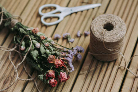 A closeup shot of twine with white scissors  and dried flowers on a wooden surfaceの写真素材