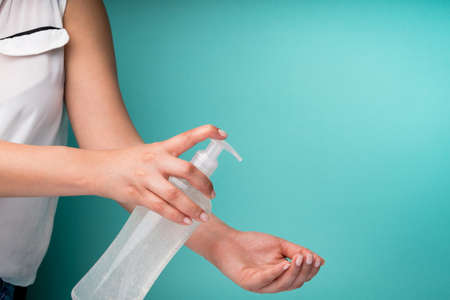 A closeup of a woman applying hand sanitizer against Coronavirus on a turquoise background