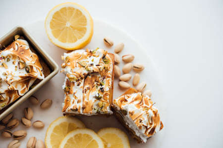 An overhead wide shot of tasty cake dessert with nuts and lemons on a white plate and white...