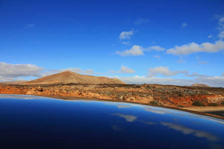 A beautiful shot of sea near deserted hills and mountains in the distance under a blue skyの写真素材