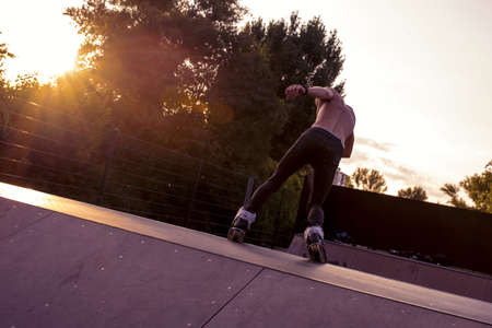 A young male rollerblading in a park surrounded by trees under the sunlightの写真素材