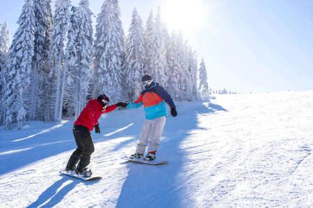 Two snowboarders holding hands while riding down the hillの写真素材