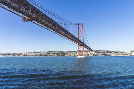 A low angle shot of a Ponte 25 de Abril bridge over the water with the  city in the distanceの写真素材