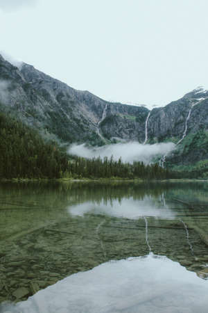 A vertical shot of the Avalanche Lake near a forest with a mountain in the background at Glacier National Park, Montana, USAの写真素材