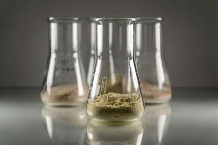 A closeup of glass chemistry flasks with brown chemical powder in them