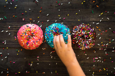 Colorful tasty sparkled donuts on a wooden background. Perfect for dessert-related post and articlesの写真素材