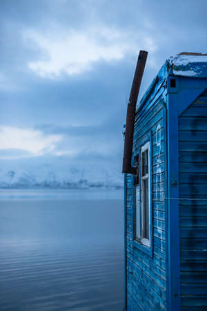 Little wooden house on a lake during winter with a chimneyの写真素材