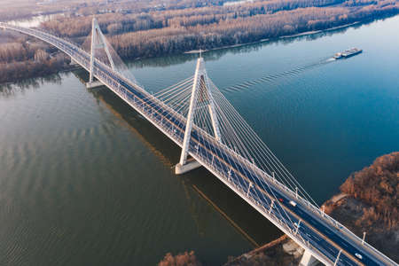 An aerial beautiful shot of a suspension bridge over a large river with a boat sailing in itの写真素材