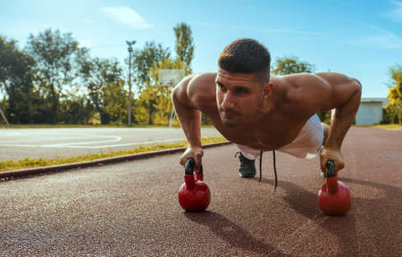 A young Caucasian muscular man working out with dumbells