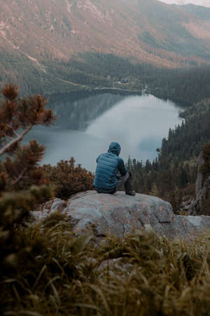 A male traveler hiking on a high rock and enjoy with mountains and cloudy skyの写真素材