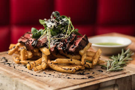 A closeup of a fries with beef and vegetable leaf on top on a wooden tray  with blurred backgroundの写真素材