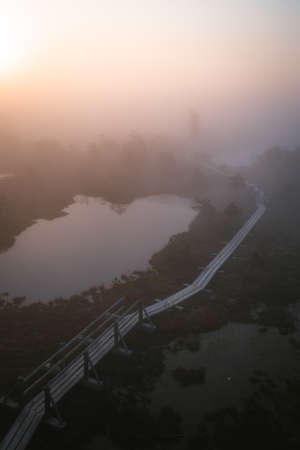 An aerial shot of a lake next to a bridge on a landscape during sunsetの写真素材