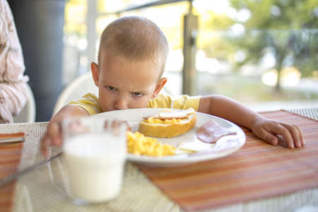 A shallow focus of an unhappy kid sitting in front of the table with food on itの写真素材
