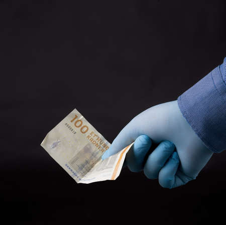 A closeup of a person in latex gloves holding hundred kroner isolated on a dark blurry backgroundの写真素材