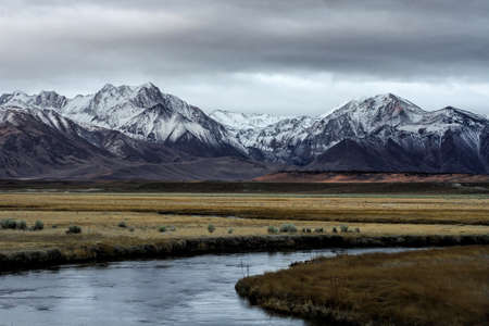A beautiful wide shot of mountains surrounded by a river and flat grass fields