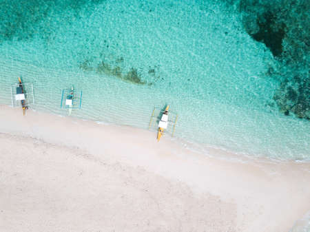 An aerial shot of a sandy beach and crystal clear water with a few boatsの写真素材
