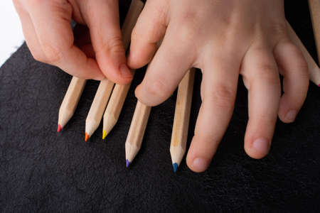 A closeup shot of a child's hands with fingers separating colorful pencilsの写真素材
