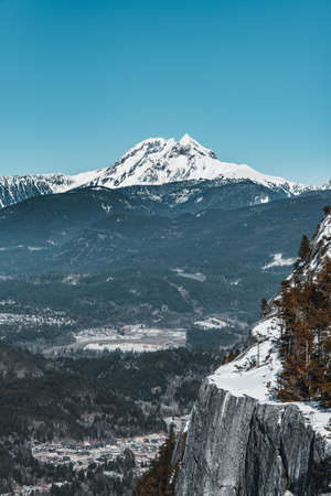 A vertical shot of a white mountain surrounded by trees and cliffs under a blue sky