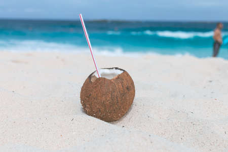 A closeup shot of a brown coconut with a straw in it on sand