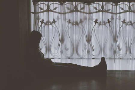 A silhouette depressed female sitting on the floor in the dark by the windowの写真素材