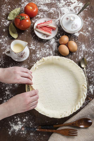 A vertical shot of a chef preparing the dough for a pie on a table next to some eggs and crab sticksの写真素材
