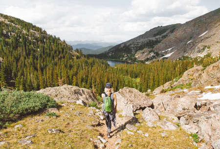 A female with backpack standing on the edge of the mountain enjoying the view of green leaf trees...