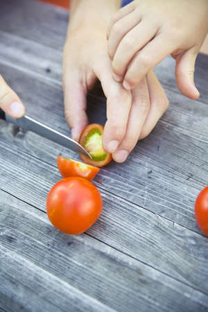 A high angle shot of a person slicing tomatoes with a small knife on a wooden surface at daytime