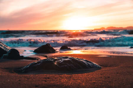 A beautiful shot of the sunset on the beach near the wavy ocean in the eveningの写真素材