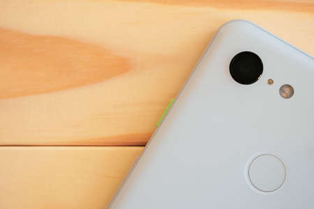 A closeup shot of white smartphone with fingerprint lock on a wooden surface