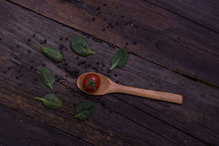 An overhead of a wooden spoon with a cherry tomato on it placed in a wooden tableの写真素材