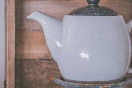 A closeup shot of a white ceramic teapot on a metal pedestal in the kitchen