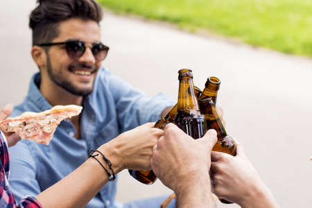 A sunny scenery of a group of caucasian friends toasting with their beer bottles in a parkの写真素材