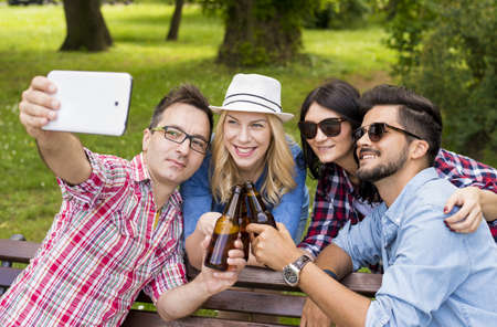 A group of young friends drinking beers and taking a selfie on a park bench