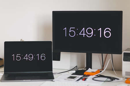 A selective shot of a black monitor screen near a black laptop on a table with time showing 15:49:16の写真素材