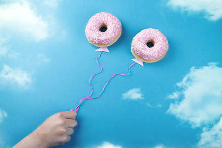 Two pink donuts on a sky background with two threads coming down from them as if they are balloonsの写真素材