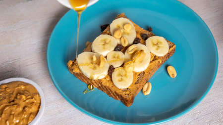 A selective closeup shot of a toast with peanut butter, various seeds, honey, and bananasの写真素材