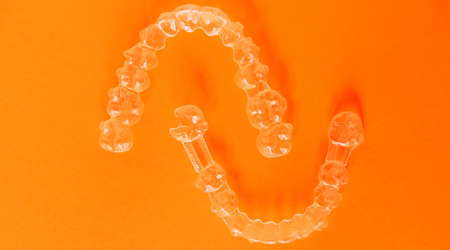 A top view of modern transparent aligners isolated on an orange background